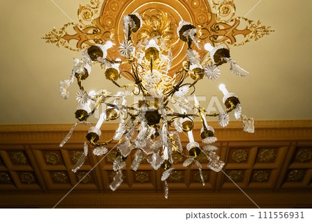 Crystal gold chandelier or luster with long electric candles on stucco ceiling. View from below Crystal gold chandelier or luster with long electric candles on stucco ceiling. View from below 111556931