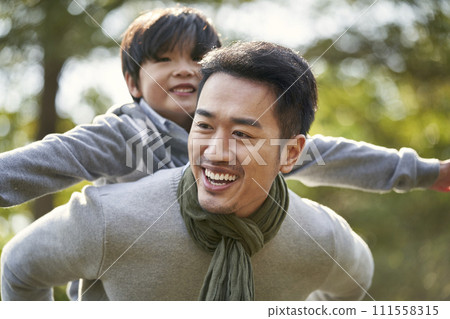 young asian father having fun carrying son on back outdoors in park 111558315