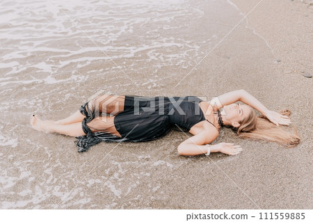 Woman summer travel sea. Happy tourist in black dress enjoy taking picture outdoors for memories. Woman traveler posing on sea beach surrounded by volcanic mountains, sharing travel adventure journey Woman summer travel sea. Happy tourist in black dress enjoy taking picture outdoors for memories. Woman traveler posing on sea beach surrounded by volcanic mountains, sharing travel adventure journey 111559885
