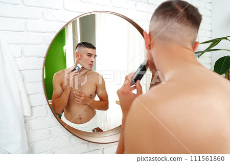 Handsome young man shaving face with electric razor on white background Handsome young man shaving face with electric razor on white background 111561860