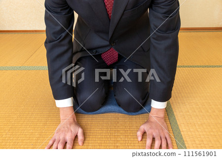 A man in a black suit apologizes with his hand on the tatami mat 111561901