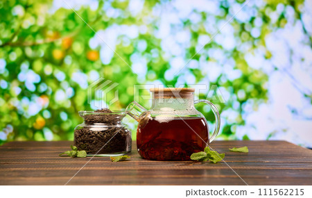 natural organic herbal tea in glass teapot and jar with dry tea on a wooden table 111562215
