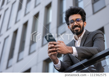 Smiling good-looking hindu man texting on the phone and feeling contented 111562575