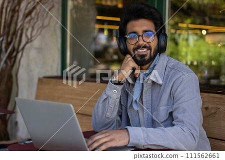 Hindu man in headphones working on a laptop and looking contented Hindu man in headphones working on a laptop and looking contented 111562661