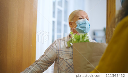 Old woman in protective face mask opening door to delivery service woman 111563432