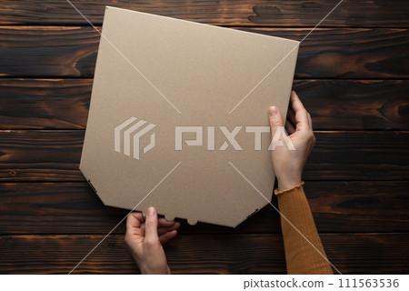 Pizza closed carton box in caucasian hands on natural dark wooden table flat lay mockup with copy space 111563536