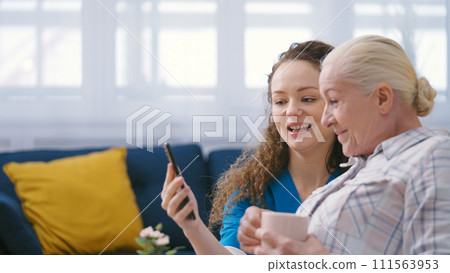 Retirement home worker helping mature woman to make a video call on smartphone Retirement home worker helping mature woman to make a video call on smartphone 111563953