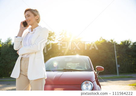 Business woman communicating on mobile phone standing near her auto door outdoors 111564222