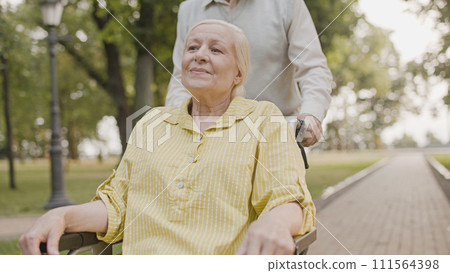 Smiling woman wheelchair user enjoying beautiful weather, resting in park with husband 111564398
