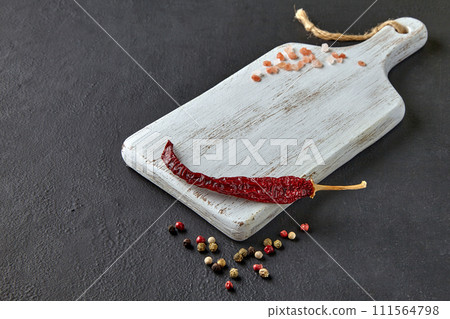 Red hot peppers, peppercorns and coarse pink salt on a white wooden cutting board on a black concrete table. Food display template Red hot peppers, peppercorns and coarse pink salt on a white wooden cutting board on a black concrete table. Food display template 111564798