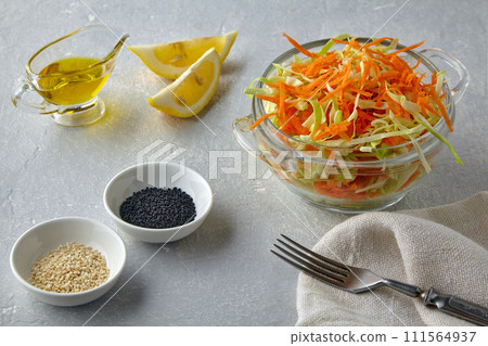 Vegetable salad of cabbage, carrots and cumin and sesame seeds dressed with olive oil and lemon in a glass bowl on a light stone table 111564937