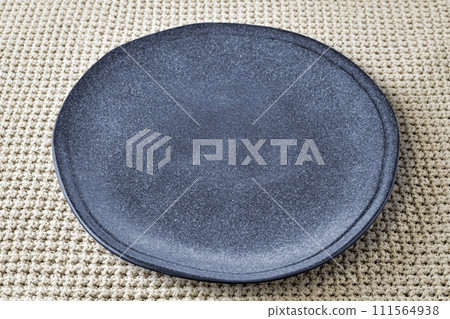 Gray ceramic plate of irregular shape on a beige knitted background 111564938