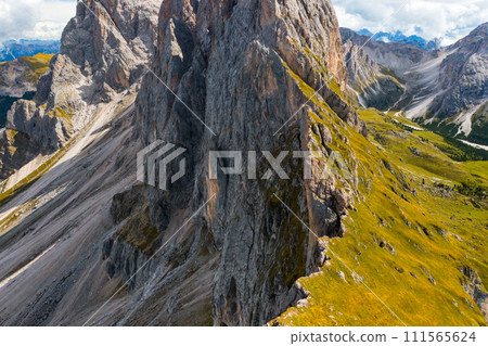 Rocky Seceda mountain range slope covered with fresh green grass in shadow. Scenic wild nature of Italian Alps on sunny summer day aerial view 111565624