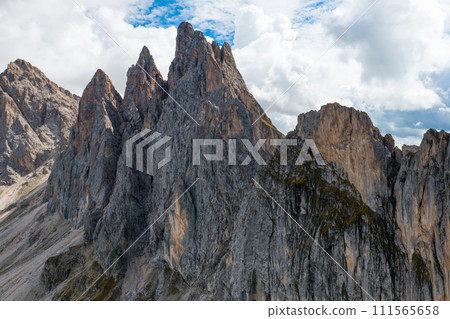 Rocky shady peak of Seceda mountain range against cloudy sky. Summit of long ridgeline in touristic Italian Alps on summer day aerial view 111565658