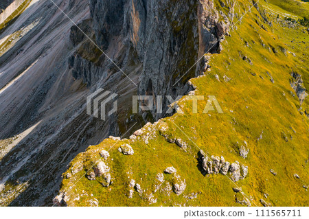 Green grass grows on steep slope of rocky Seceda mountain on sunny summer day. Rocky ridgeline in touristic Italian Alps aerial view 111565711