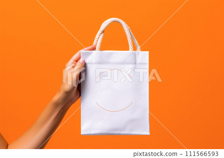 Woman's hand holding white paper shopping bag on orange background. Shopping concept. 111566593