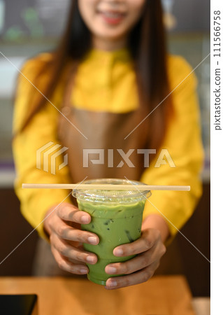 Smiling female cafe owner holding a plastic cup of iced matcha green tea latte with paper straw Smiling female cafe owner holding a plastic cup of iced matcha green tea latte with paper straw 111566758