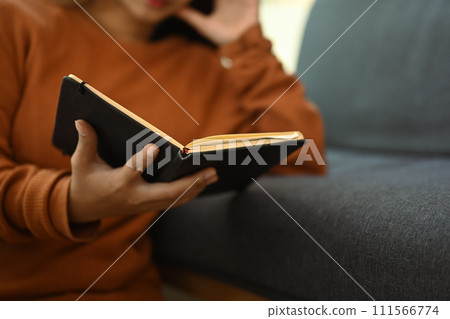 Cropped shot young woman in casual clothes reading book and spending free time at home on weekend Cropped shot young woman in casual clothes reading book and spending free time at home on weekend 111566774