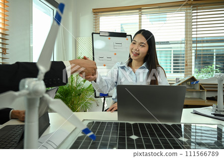 Businesspeople shaking hands after meeting with solar panel and wind turbine on table. New sustainable energy concept 111566789