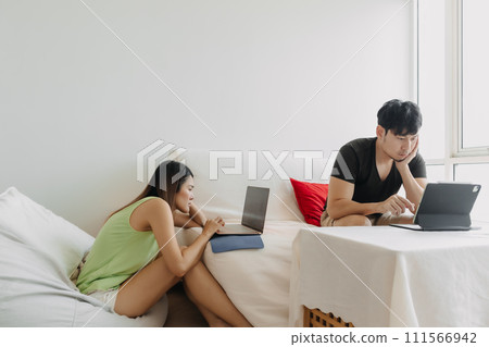 Asian Thai couple using laptop, Both man and woman busy working on notebook, lover freelancer sitting on couch in room apartment. 111566942