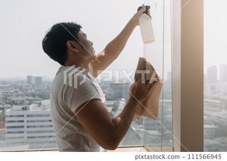 Backside view of asian Thai man wiping window glass in room apartment with city view, keep glass sparking clean, housework concept. 111566945