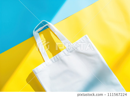 Advertising shot from above of white fabric reusable eco shopper, shopping bag on blue and yellow background 111567224