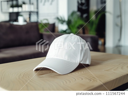 Advertising mockup shot of white denim cap lying on light wooden table with brown sofa and green plant at the background Advertising mockup shot of white denim cap lying on light wooden table with brown sofa and green plant at the background 111567244
