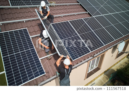 Man technician building photovoltaic solar moduls on roof of house. Mounter in helmet installing solar panel system outdoors. Concept of alternative and renewable energy. Aerial view. 111567518