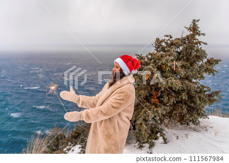 Outdoor winter portrait of happy smiling woman, light faux fur coat holding heart sparkler, posing against sea and snow background Outdoor winter portrait of happy smiling woman, light faux fur coat holding heart sparkler, posing against sea and snow background 111567984