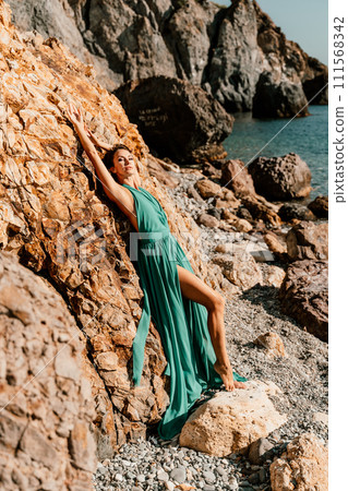 Woman green dress sea. Woman in a long mint dress posing on a beach with rocks on sunny day. Girl on the nature on blue sky background. 111568342