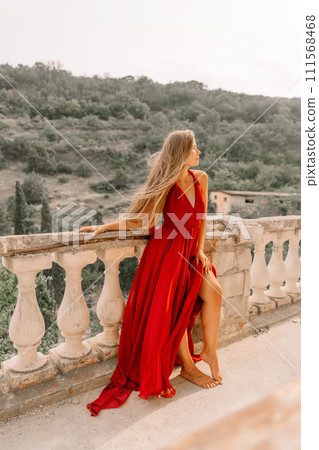 Woman red dress. Summer lifestyle of a happy woman posing near a fence with balusters over the sea. 111568468