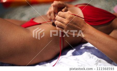 Woman taking red bikini off on beach for tan, lady stripping holiday swimsuit with bow in string. Fun and relax, sexy model untying swimming costume bra, happy woman in swimwear on vacation Woman taking red bikini off on beach for tan, lady stripping holiday swimsuit with bow in string. Fun and relax, sexy model untying swimming costume bra, happy woman in swimwear on vacation 111568593