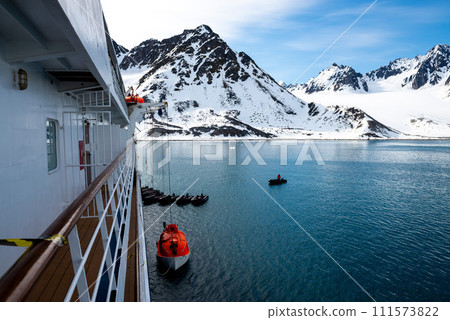 Lowering orange lifeboat to water in Arctic waters, Svalbard. Abandon ship drill. Lifeboat training. Man over board drill. Lowering orange lifeboat to water in Arctic waters, Svalbard. Abandon ship drill. Lifeboat training. Man over board drill. 111573822
