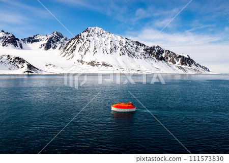 Maneuvering orange lifeboat in water in Arctic waters, Svalbard. Abandon ship drill. Lifeboat training. Man over board drill. Maneuvering orange lifeboat in water in Arctic waters, Svalbard. Abandon ship drill. Lifeboat training. Man over board drill. 111573830