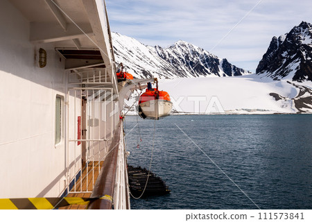 Lowering orange lifeboat to water in Arctic waters, Svalbard. Abandon ship drill. Lifeboat training. Man over board drill. 111573841