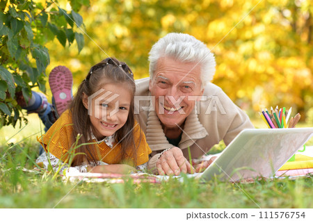 Grandfather and granddaughter drawing and using laptop in autumn park 111576754