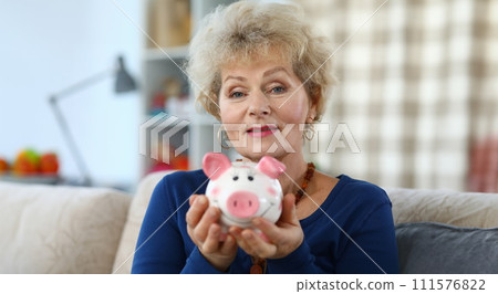 Happy elderly woman shows pink ceramic piggy bank 111576822