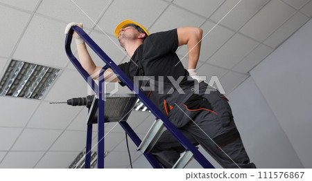 Repairman ladder with drill and looks at ceiling 111576867