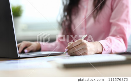 Woman makes notes with pen on sheet and on laptop 111576873