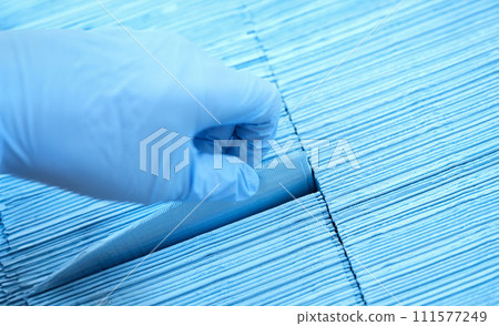 Doctor hand in rubber gloves pulling out sterile disposable napkin from packaging closeup 111577249