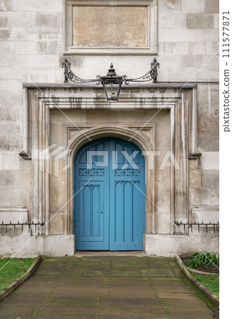 Arched medieval door with a lantern above it. Details of Closed blue wooden church doorway in a gothic stone wall. Arched medieval door with a lantern above it. Details of Closed blue wooden church doorway in a gothic stone wall. 111577871