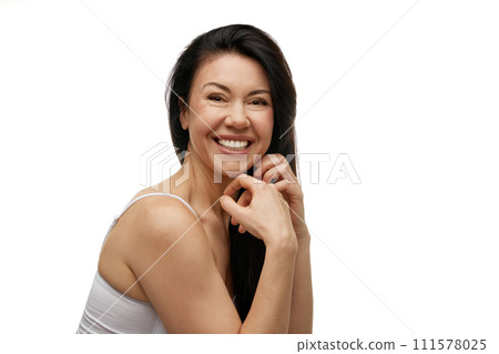 Middle aged woman laughing holding hands under chin and looking at camera against white studio background. 111578025