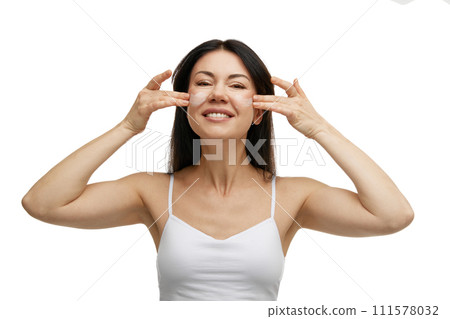 Portrait of happy brunette woman applies moisturized cosmetic product for facial skin against white studio background. 111578032