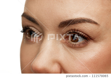 Cropped portrait of middle-aged woman with well kept skin against white studio background. Model without wrinkles in periorbital area. 111578065