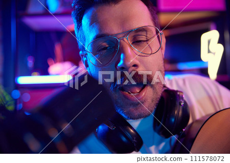 Close up photo of joyful young man, artist creating music with acoustic guitar in vibrant, lighting recording space. Close up photo of joyful young man, artist creating music with acoustic guitar in vibrant, lighting recording space. 111578072