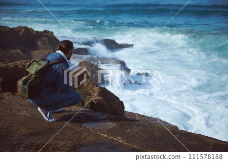 Absorbed male traveler with backpack, admiring the dangerous splashing waves from a rocky cliff Absorbed male traveler with backpack, admiring the dangerous splashing waves from a rocky cliff 111578188