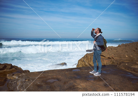 Full length portrait of male tourist hiker looking into distance, discovering beautiful nature, standing on rock by sea 111578194