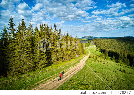 Cyclist man riding electric mountain bike outdoors on sunny day. Male tourist biking along grassy trail in the mountains, wearing helmet and backpack. Concept of sport, active leisure and nature. Cyclist man riding electric mountain bike outdoors on sunny day. Male tourist biking along grassy trail in the mountains, wearing helmet and backpack. Concept of sport, active leisure and nature. 111578237