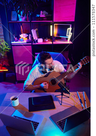 High angle view portrait of focused man in glasses producing acoustic melodies in colorful, illuminated workspace. High angle view portrait of focused man in glasses producing acoustic melodies in colorful, illuminated workspace. 111578347