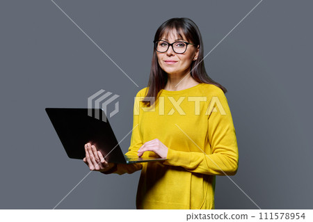 Middle-aged woman using laptop computer on gray studio background 111578954